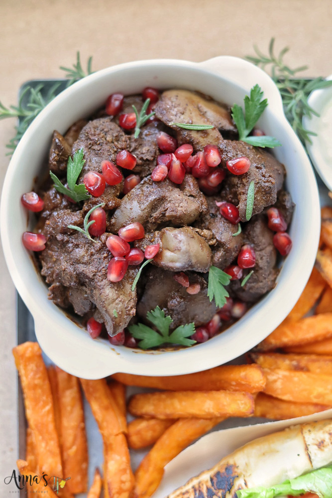 Lebanese chicken livers mezza garnished with pomegranate seeds and fresh rosemary and parsley leaves and served with some sweet potato fries as side